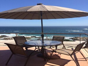 A round table with four chairs and a large umbrella, overlooking a rocky coastline and the ocean. - Departamento Atala 5 Personas Maitencillo (Puchuncavi)