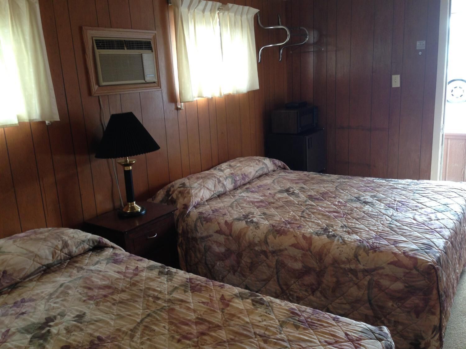 Una habitación con dos camas, una mesita de noche, una lámpara, un calefactor y una ventana con cortinas.