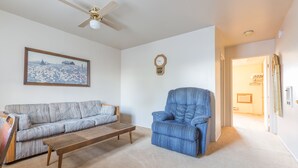 A living room with a sofa, a blue armchair, a wooden coffee table, a ceiling fan, a clock, and a framed picture on the wall. - Dayton Motel (Dayton)