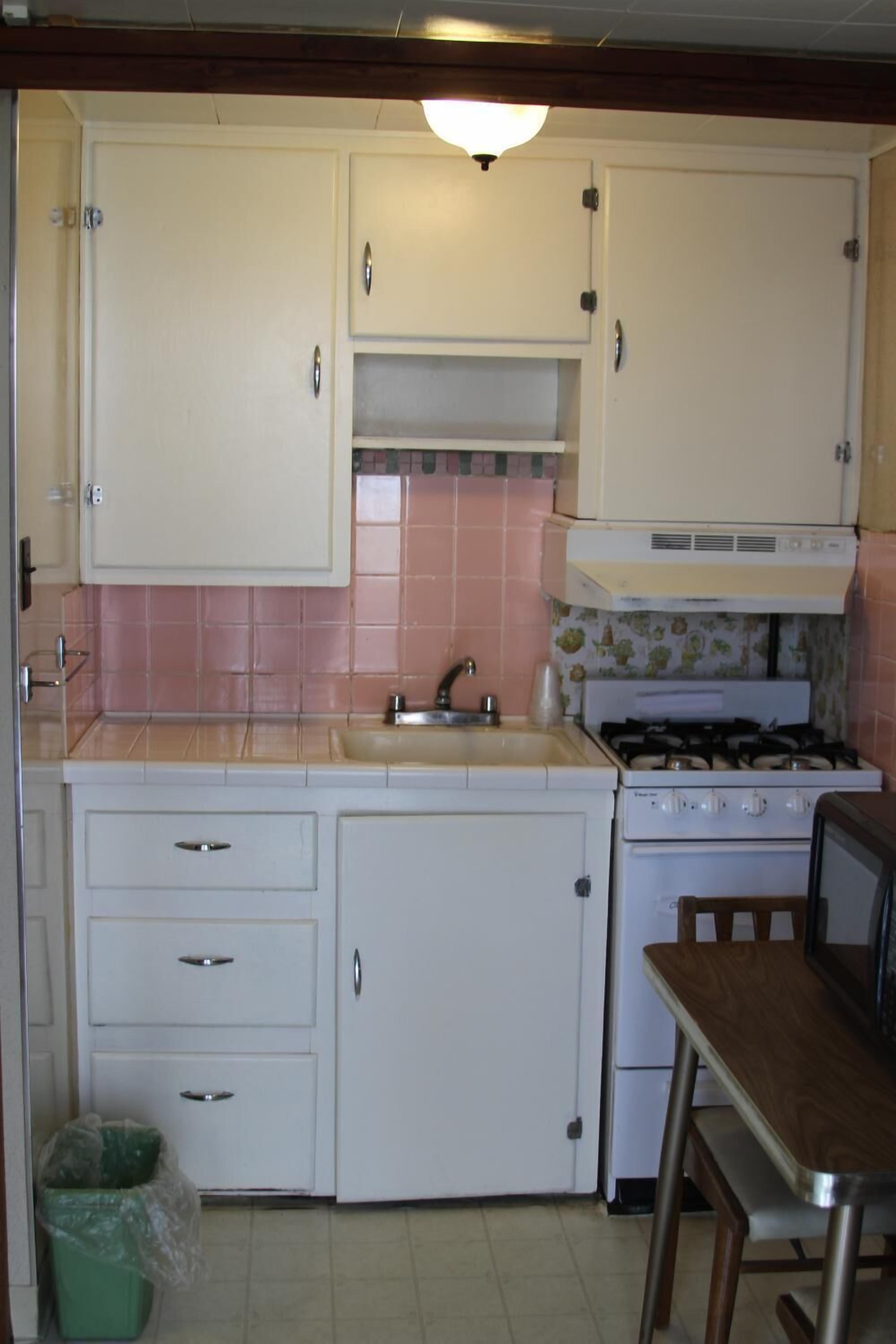 Una cocina compacta con armarios blancos, estufa y lavabo.