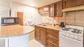 A kitchen with wooden cabinets, a microwave, a stove, and a sink. - Dayton Motel (Dayton)