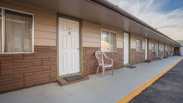 A row of motel rooms with individual doors numbered 7 to 8, a single chair outside, and a clear sky.