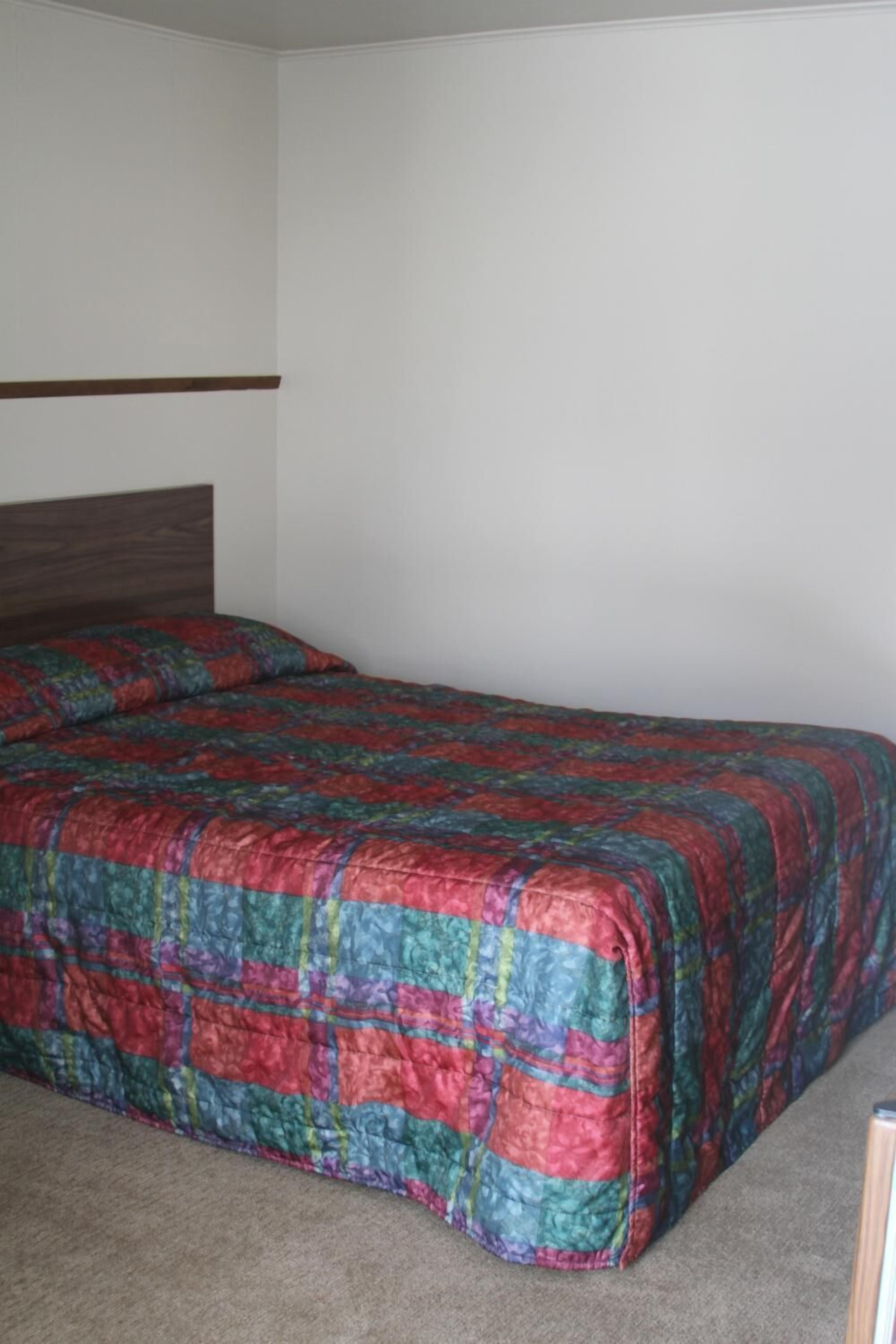 A single bed with a colorful quilt in a room with plain white walls and a wooden headboard.