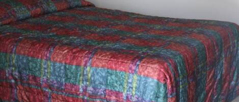 A single bed with a colorful quilt in a room with plain white walls and a wooden headboard.