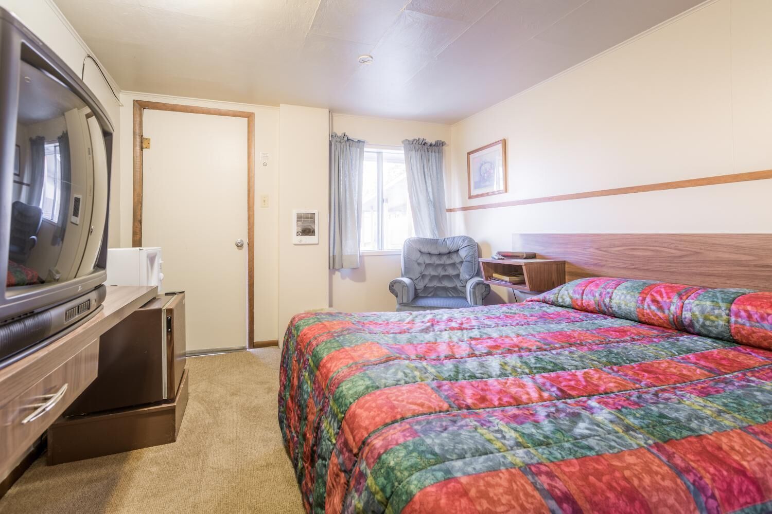 A hotel room with a bed, a chair, a television, and a small table.