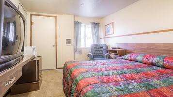 A hotel room with a bed, a chair, a television, and a small table.