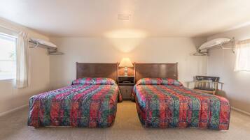 Una habitación con dos camas, una mesita de noche con lámpara, una silla y una ventana con cortinas.
