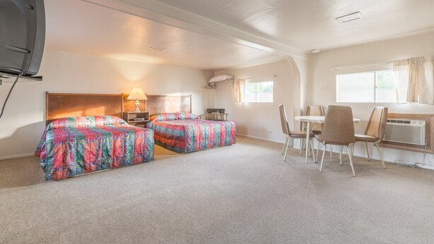 A room with two beds, a table, chairs, a lamp, and a radiator. - Dayton Motel (Dayton)