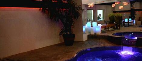 A spa area with a large potted plant, a reception desk, and a pool with illuminated edges.