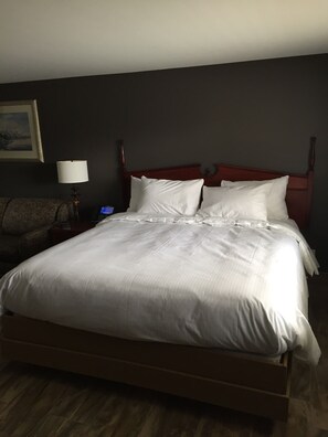 A hotel room with a large bed, a wooden headboard, a nightstand with a lamp, and a framed picture on the wall. - Wigle's Motel (Leamington)
