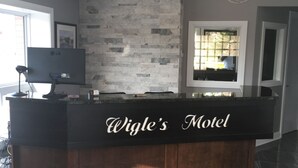 Un comptoir d’accueil portant l’inscription « Wigle’s Motel », avec un mur en pierre en arrière-plan, un lustre et une grande fenêtre avec des stores.