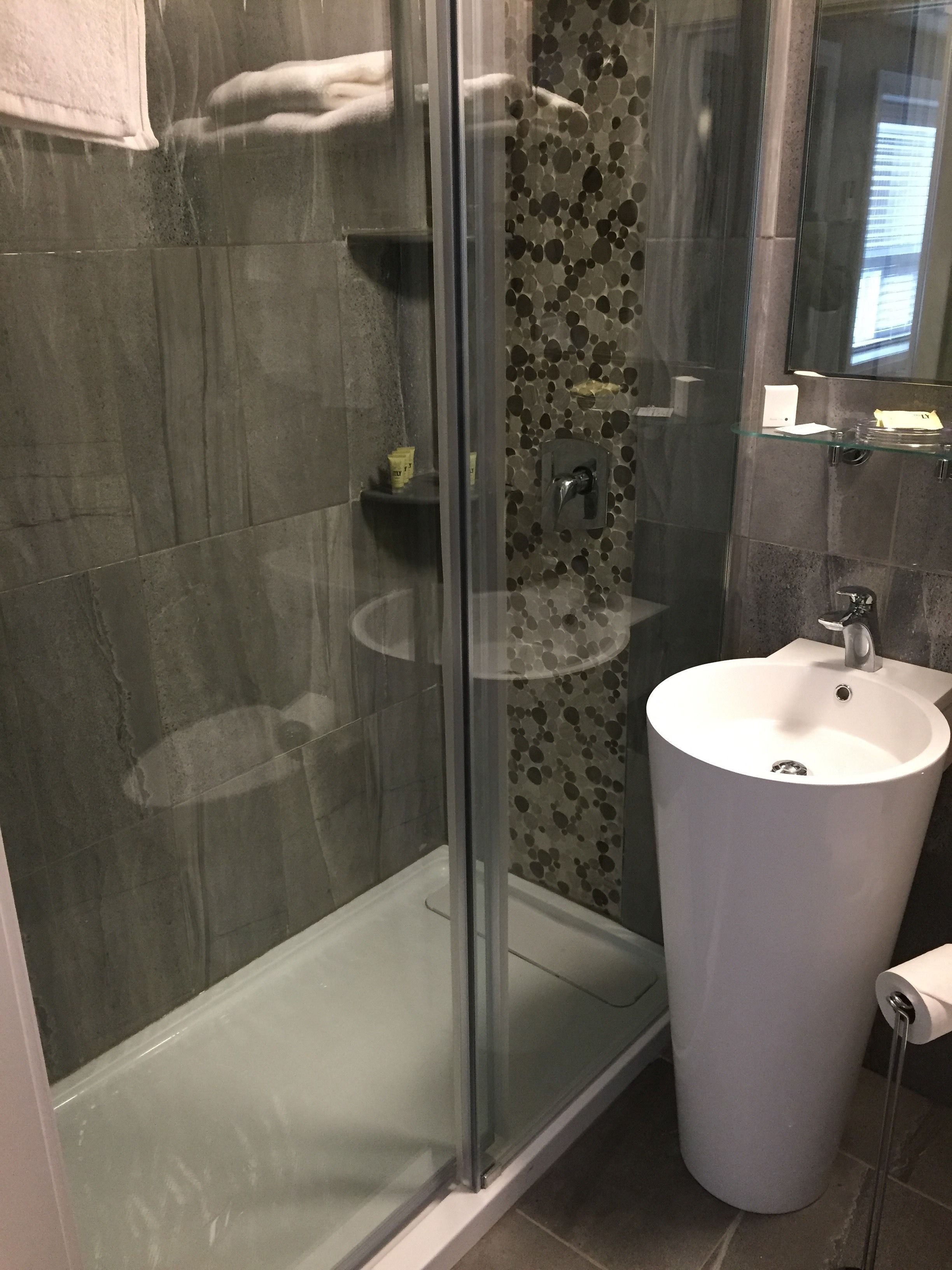 A modern bathroom with a glass shower enclosure, a white pedestal sink, and a tiled shower wall.