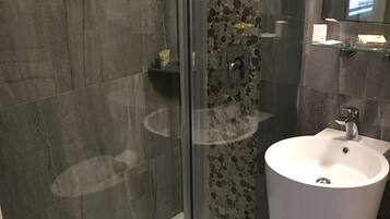 A modern bathroom with a glass shower enclosure, a white pedestal sink, and a tiled shower wall.