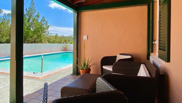 Un espace extérieur aménagé, abrité et doté de mobilier en osier, avec une piscine et une vue sur le paysage environnant.
