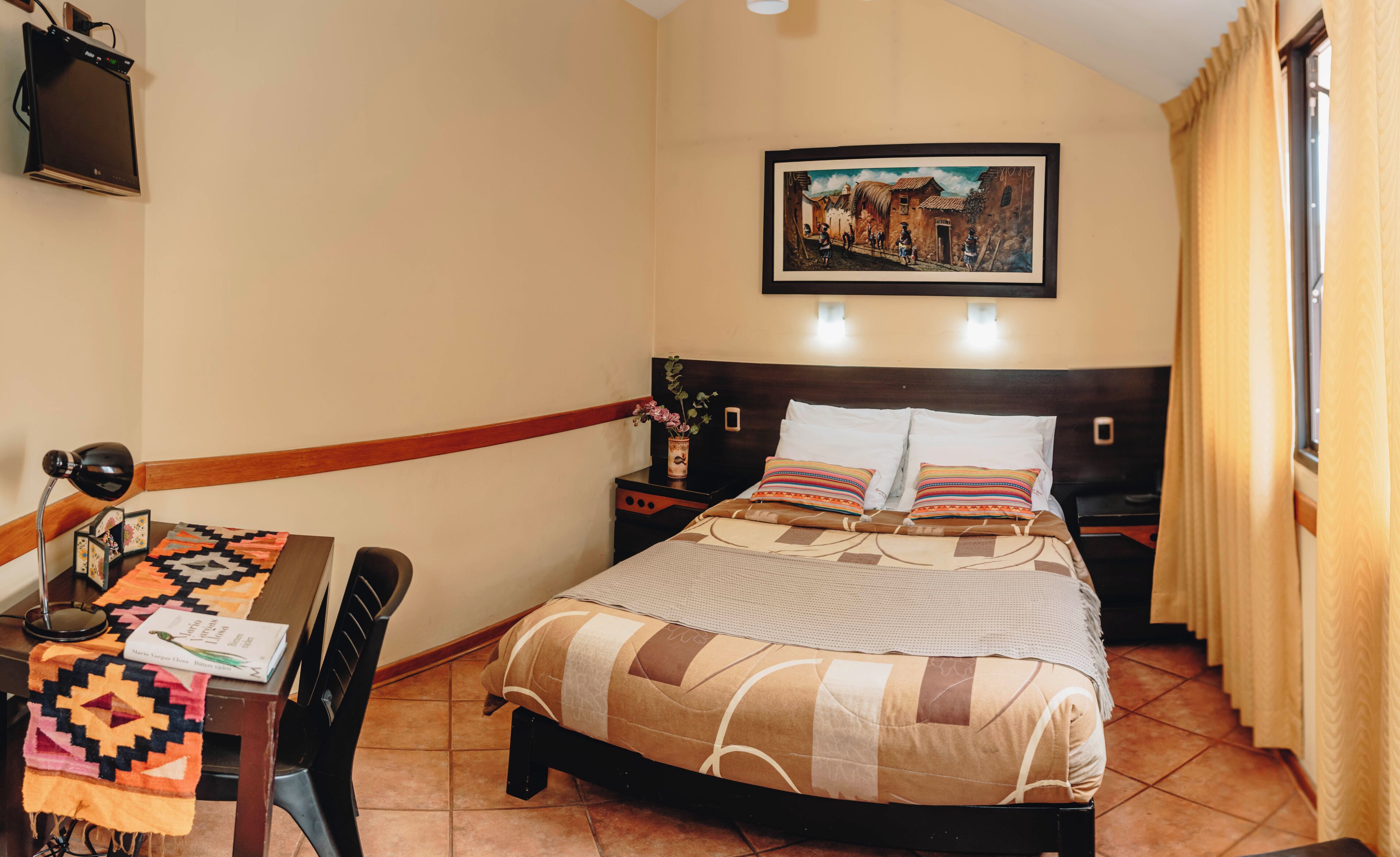 A bedroom with a bed, bedside tables, a desk, a chair, a painting on the wall, and a window with curtains.