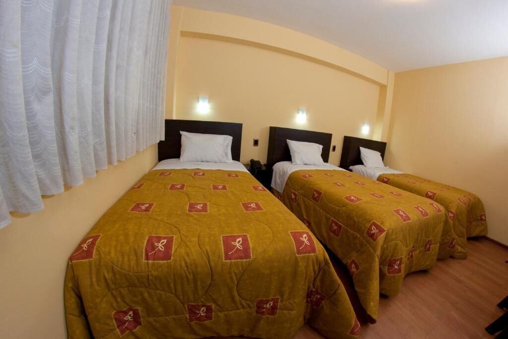 A hotel room with three beds, each with a brown bedspread and white pillows. There is a white curtain on the left side of the room.