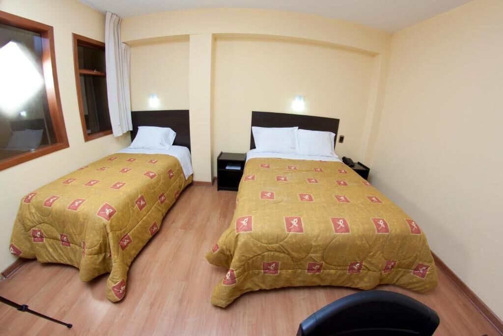 A hotel room with two single beds, each with a headboard, bedside tables, and a window with curtains.