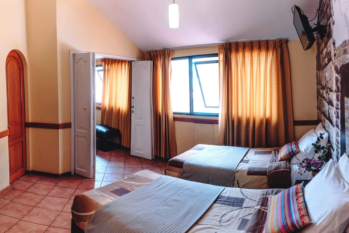 A hotel room with two beds, a wardrobe, a bench, and a window with curtains.