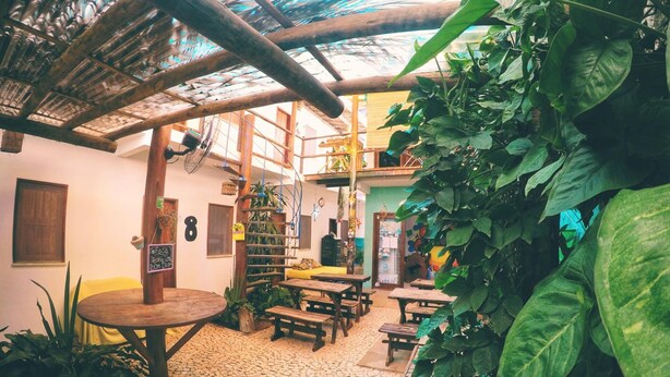 An indoor space with a rustic wooden ceiling, stone flooring, and various seating arrangements. - Buddy's Hostel e Pousada (Itacaré)