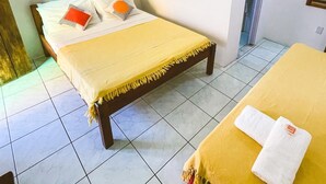 A bedroom with a bed, a bedside table, a wall-mounted light, and a door leading to another room. - Buddy's Hostel e Pousada (Itacaré)