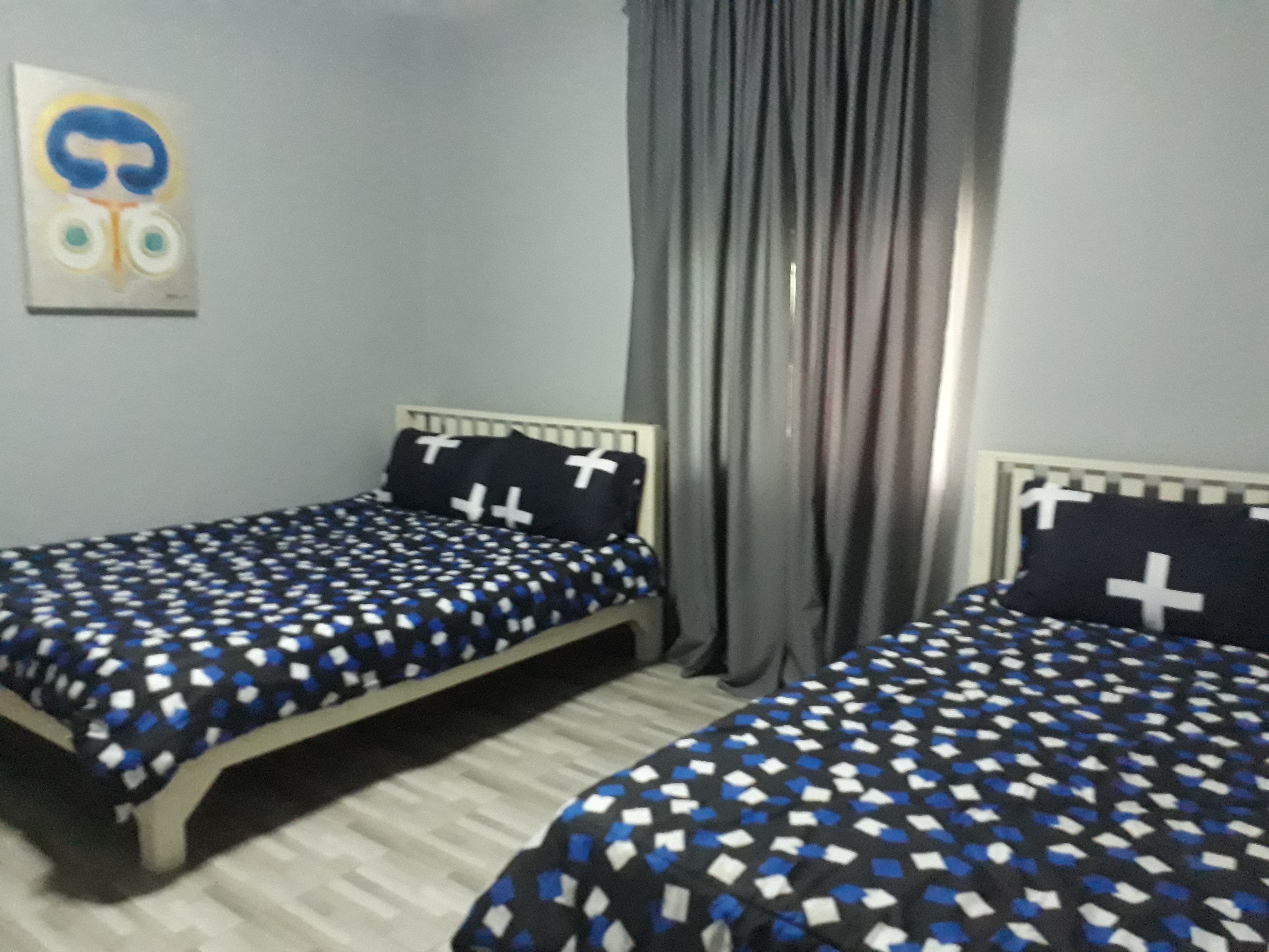 Une chambre à coucher avec deux lits, chacun recouvert d’une couvre-lit à motifs et agrémenté d’oreillers ornés de croix.