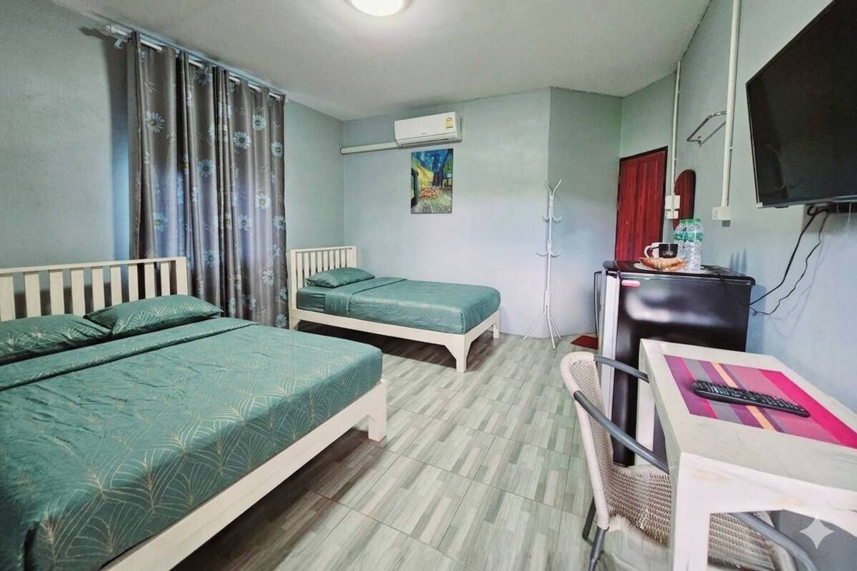 A room with two beds, a desk, a chair, an air conditioning unit, and a television.