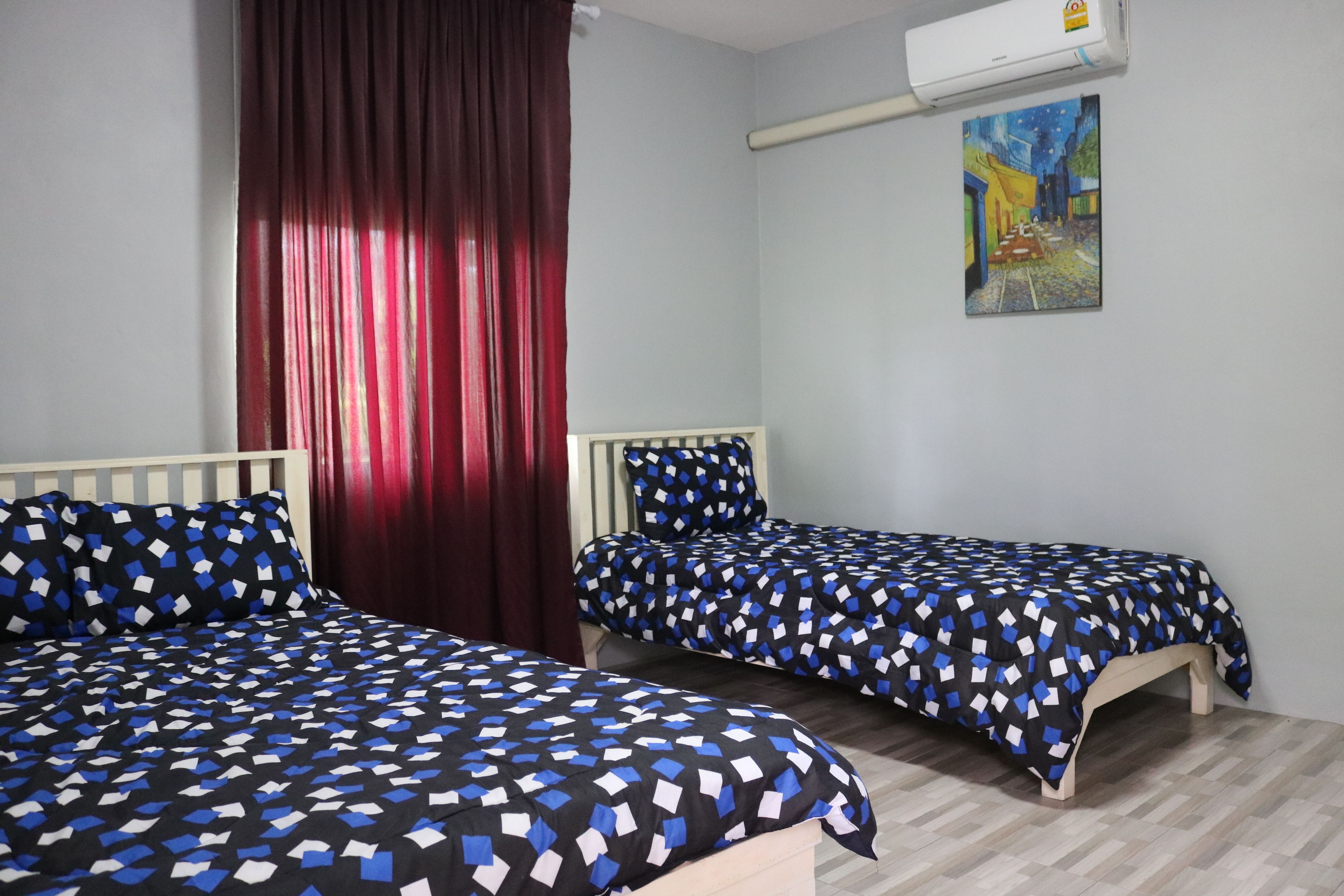 Une chambre avec deux lits, un rideau rouge, un tableau au mur et un appareil de climatisation.