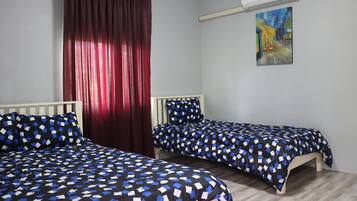 Une chambre avec deux lits, un rideau rouge, un tableau au mur et un appareil de climatisation.