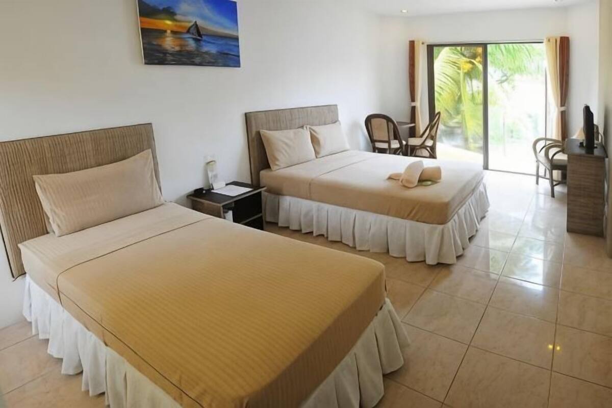 A hotel room with two beds, a desk, chairs, and a view of palm trees.