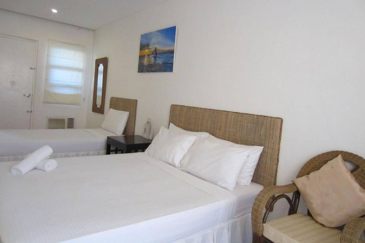 A hotel room with two beds, a chair, a painting, and a window with blinds.