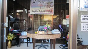 A reception desk with a sign for Boracay's White Coral Hotel, a phone number for inquiries, and a window with a view of the beach. - White Coral Hotel (Boracay Island)