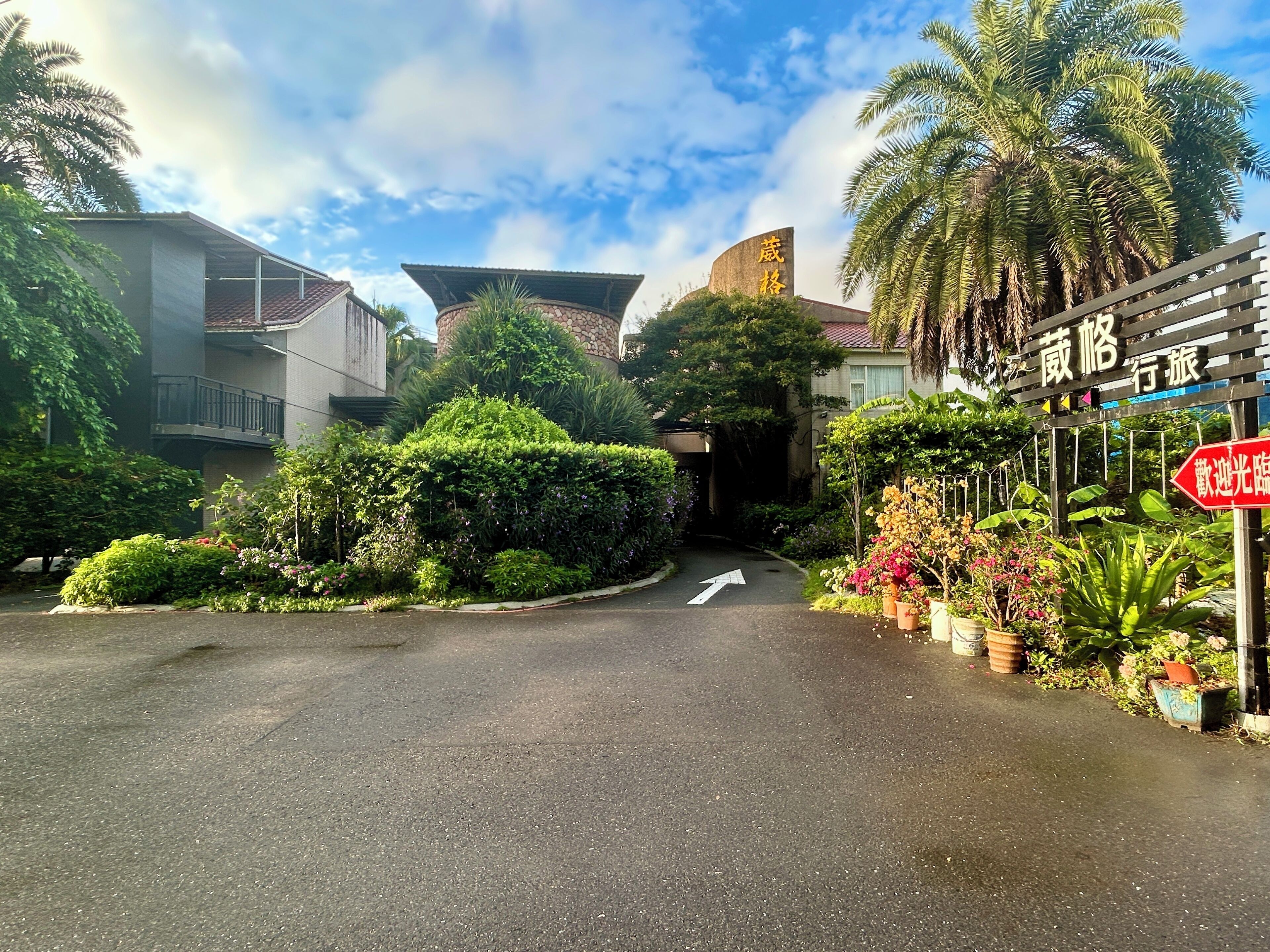 A street entrance with a directional arrow, lush greenery, and a building with a stone facade.