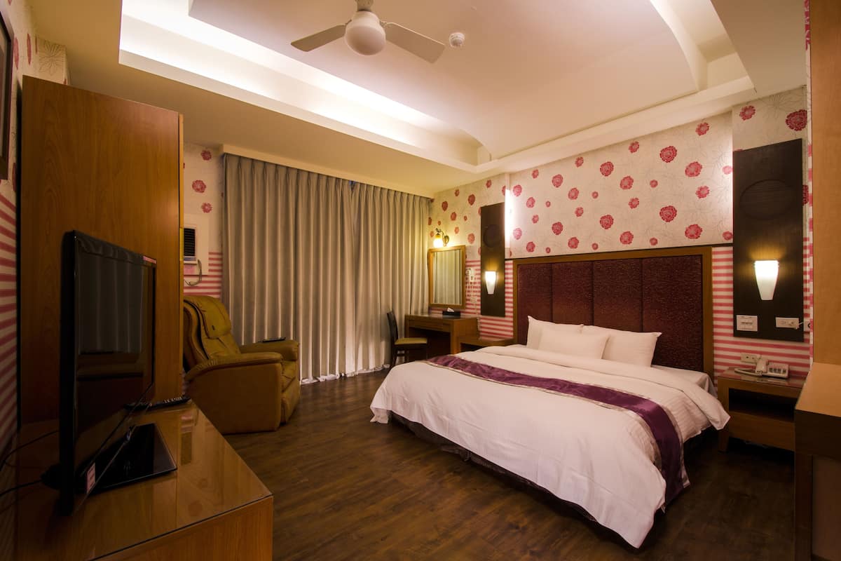 Una habitación de hotel con cama, escritorio, silla, televisor y ventilador de techo.