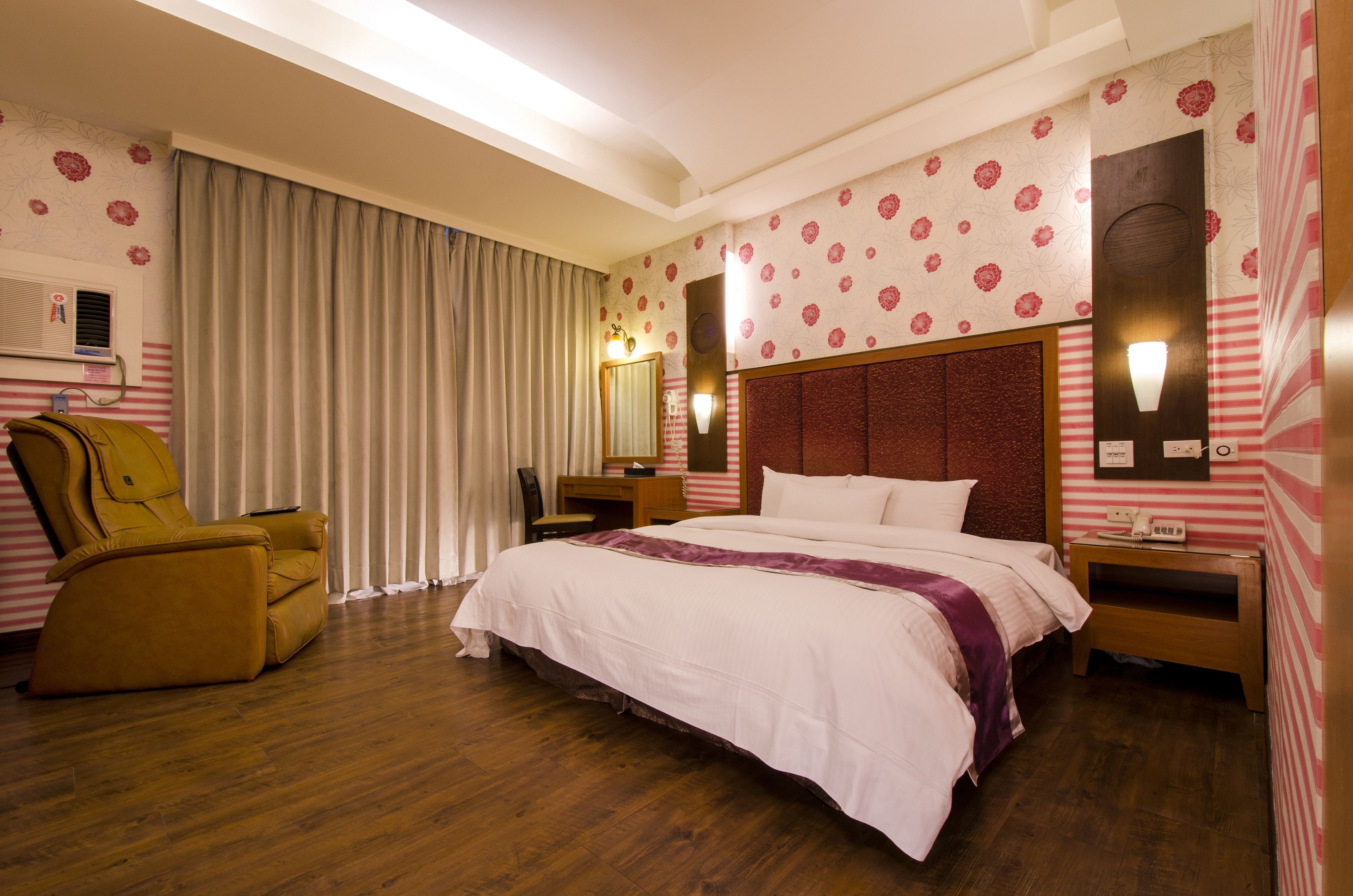 A hotel room with a large bed, a yellow armchair, a desk, and a mirror.