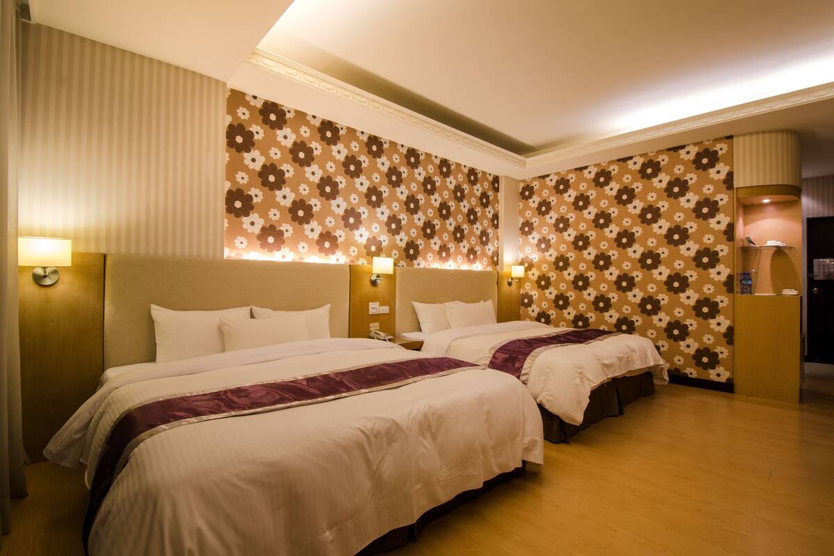 Habitación de hotel con dos camas, papel tapiz floral y lámparas de noche.
