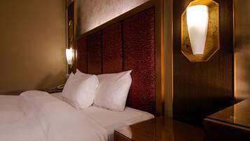 A hotel room with a large bed, a wooden headboard, a nightstand with a lamp, and a wall-mounted light fixture.