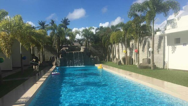 A swimming pool with clear blue water, surrounded by palm trees and a stone waterfall feature. - Shore Time Hotel Javier Leyte (Javier)