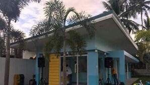 A modern building with a blue and yellow facade, large windows, and a covered entrance area with speakers and a tripod. - Shore Time Hotel Javier Leyte (Javier)