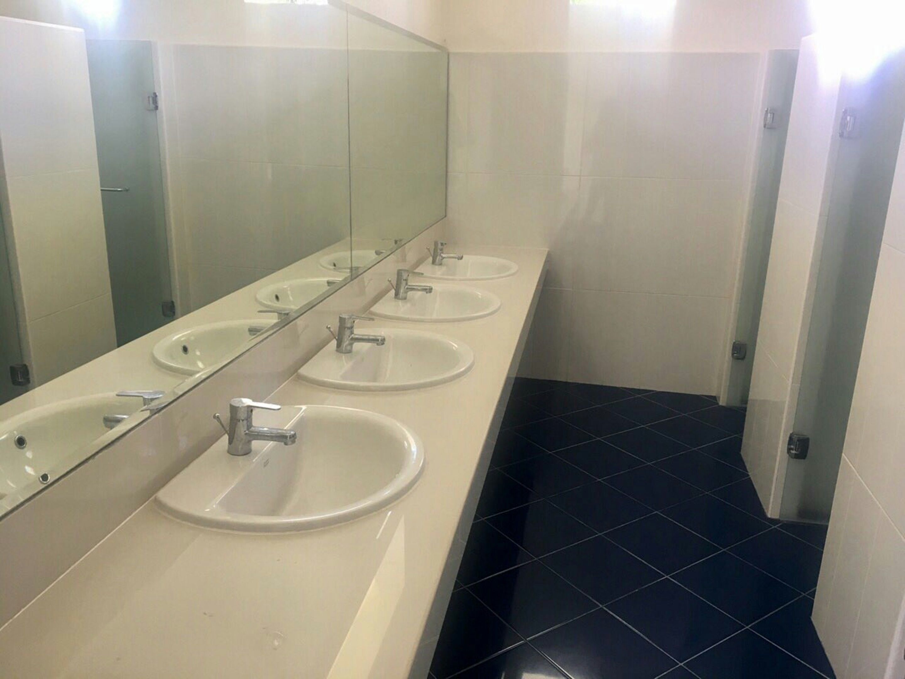 Un baño con cuatro lavamanos, un espejo grande y suelo de baldosas negras.