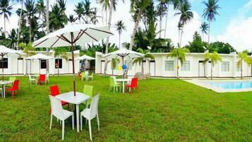 A row of white cabins with outdoor seating and a pool.