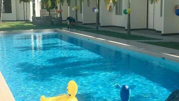 Une piscine à l’eau d’un bleu cristallin, entourée de bâtiments blancs et de palmiers.
