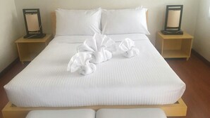 A neatly made bed with white linens and decorative towels, two bedside tables with lamps, and a wooden headboard. - Shore Time Hotel Javier Leyte (Javier)