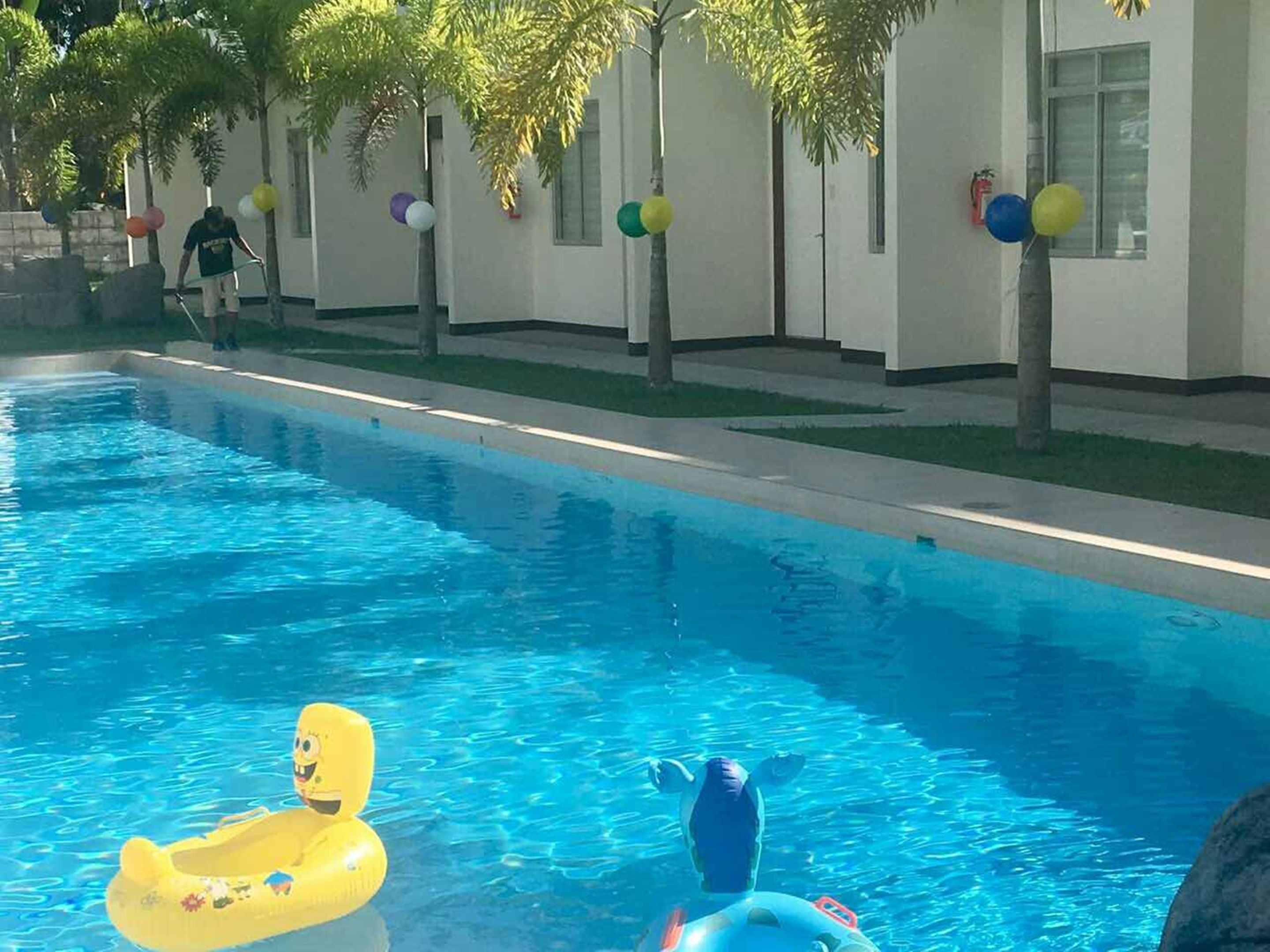 Una piscina con giochi gonfiabili, una persona sullo sfondo e un edificio decorato con palloncini.