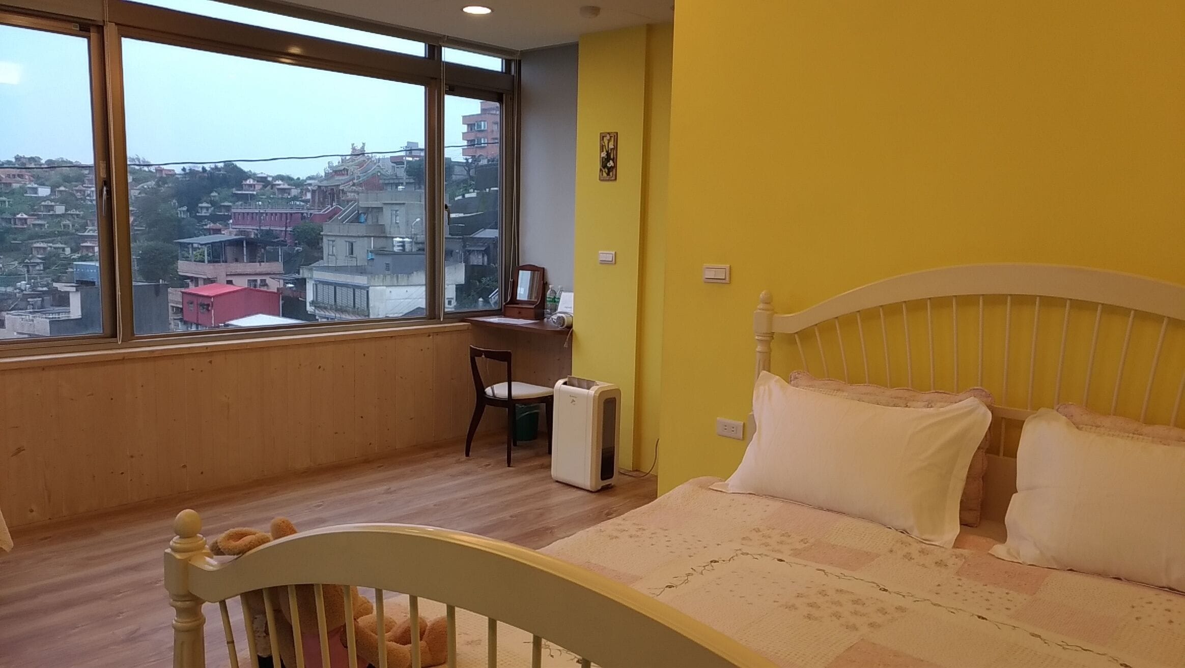 A bedroom with a large window, a bed, a desk, and a chair.