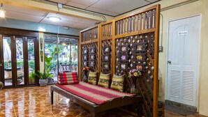 A traditional wooden bench with cushions, a decorative wall with framed pictures, and a door labeled "Toilets". - Banchan Hostel (Ayutthaya)