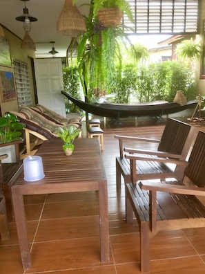 A room with a wooden table, chairs, a hammock, and potted plants. - Banchan Hostel (Ayutthaya)