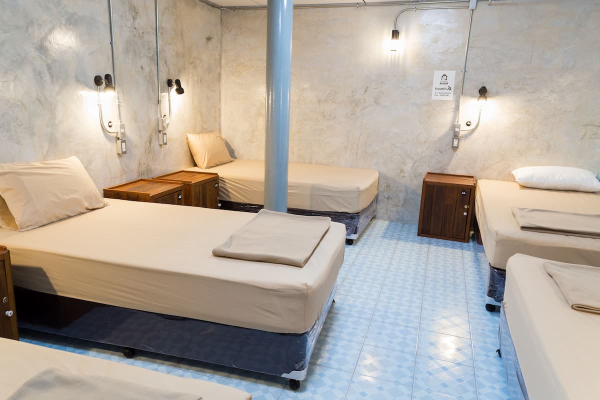 A hotel room with a large bed, two smaller beds, a wooden cabinet, and a blue pillar.