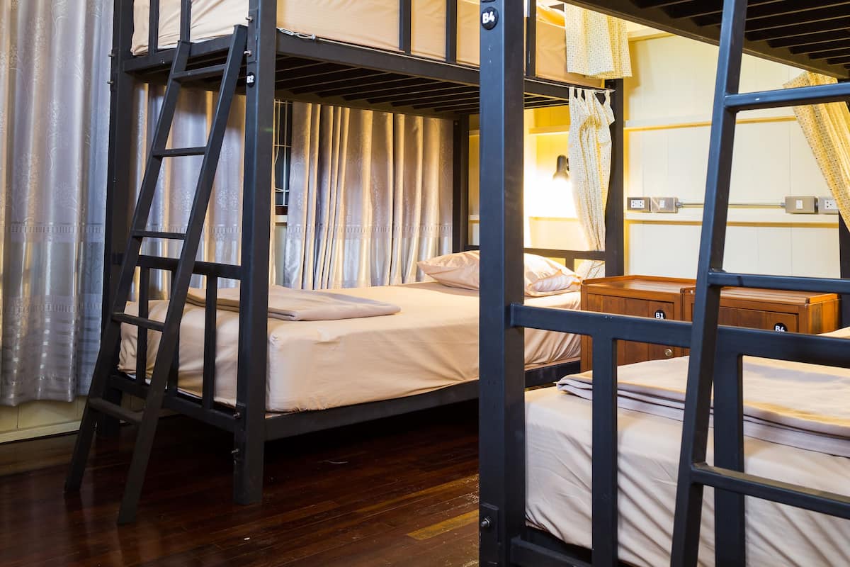 A bunk bed room with wooden flooring, a ladder, and a bedside table.