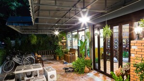 An outdoor patio area with a brick floor, potted plants, a wooden bench, and a table. - Banchan Hostel (Ayutthaya)