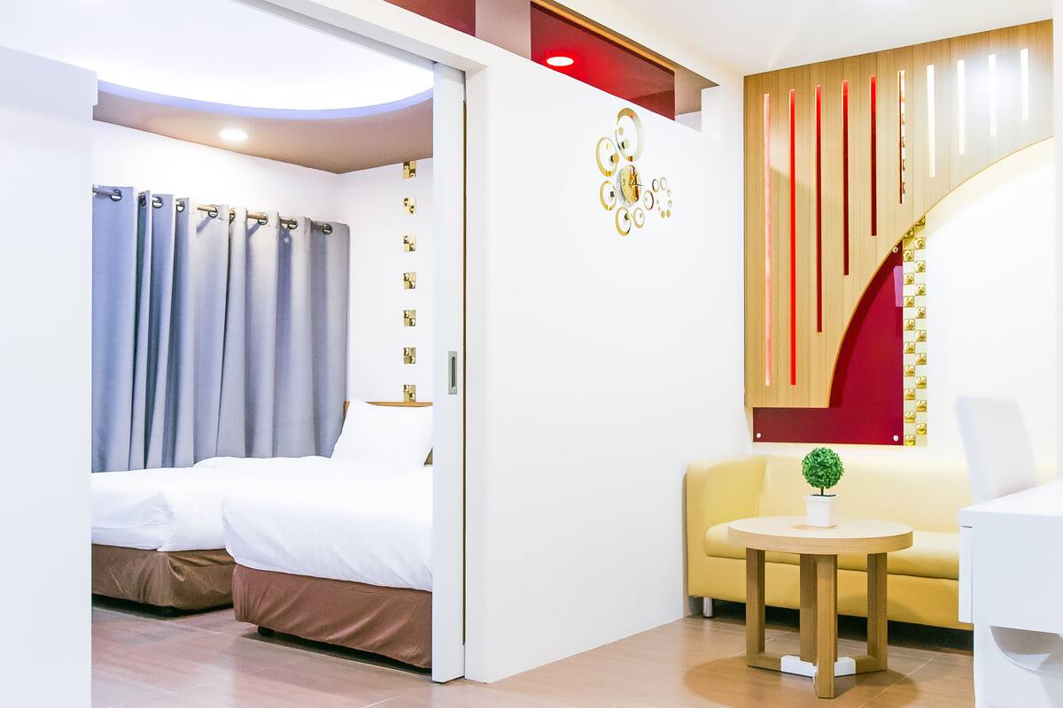 A modern hotel room with a bed, a sofa, a small table, and a decorative wall piece.